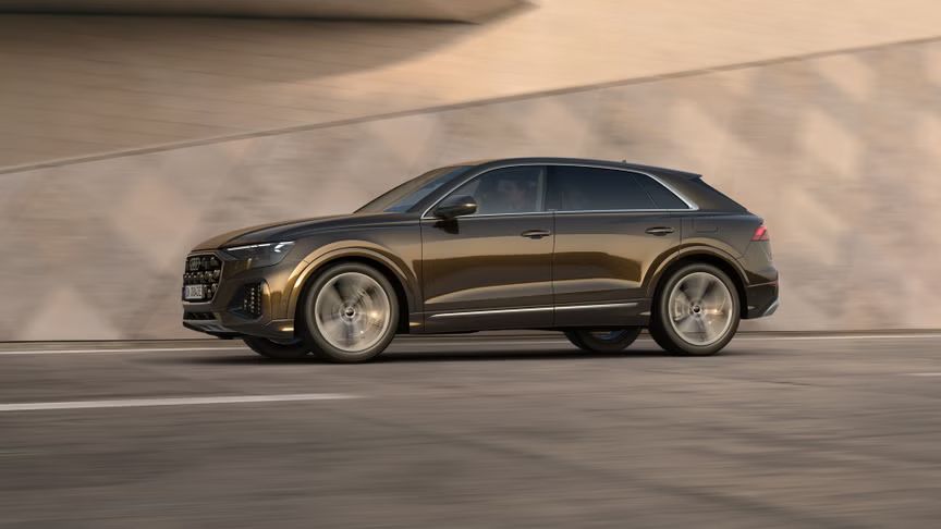 Der Q8 SUV e-hybrid von der Seite in voller Fahrt vor einem futuristischen Gebäude.