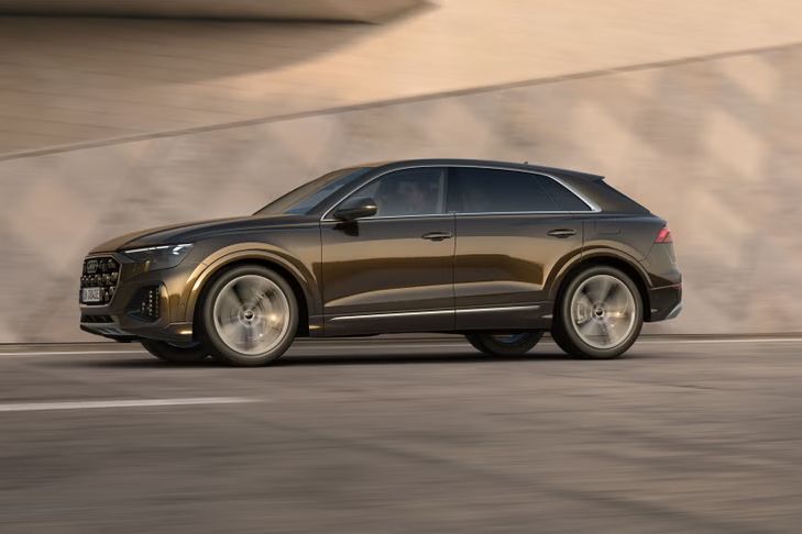 Der Q8 SUV e-hybrid von der Seite in voller Fahrt vor einem futuristischen Gebäude.