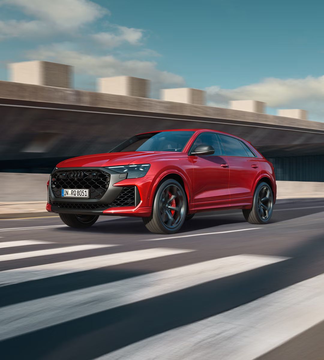 Der RS Q8 SUV performance schräg von vorn nähert sich einem Zebrastreifen. Rechts daneben ein futuristisches Gebäude in Betonoptik.