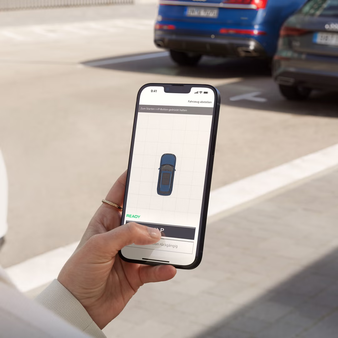 Eine junge Frau hält ein Smartphone in der Hand, auf dem ein stilisierter Audi in Draufsicht zu erkennen ist. 