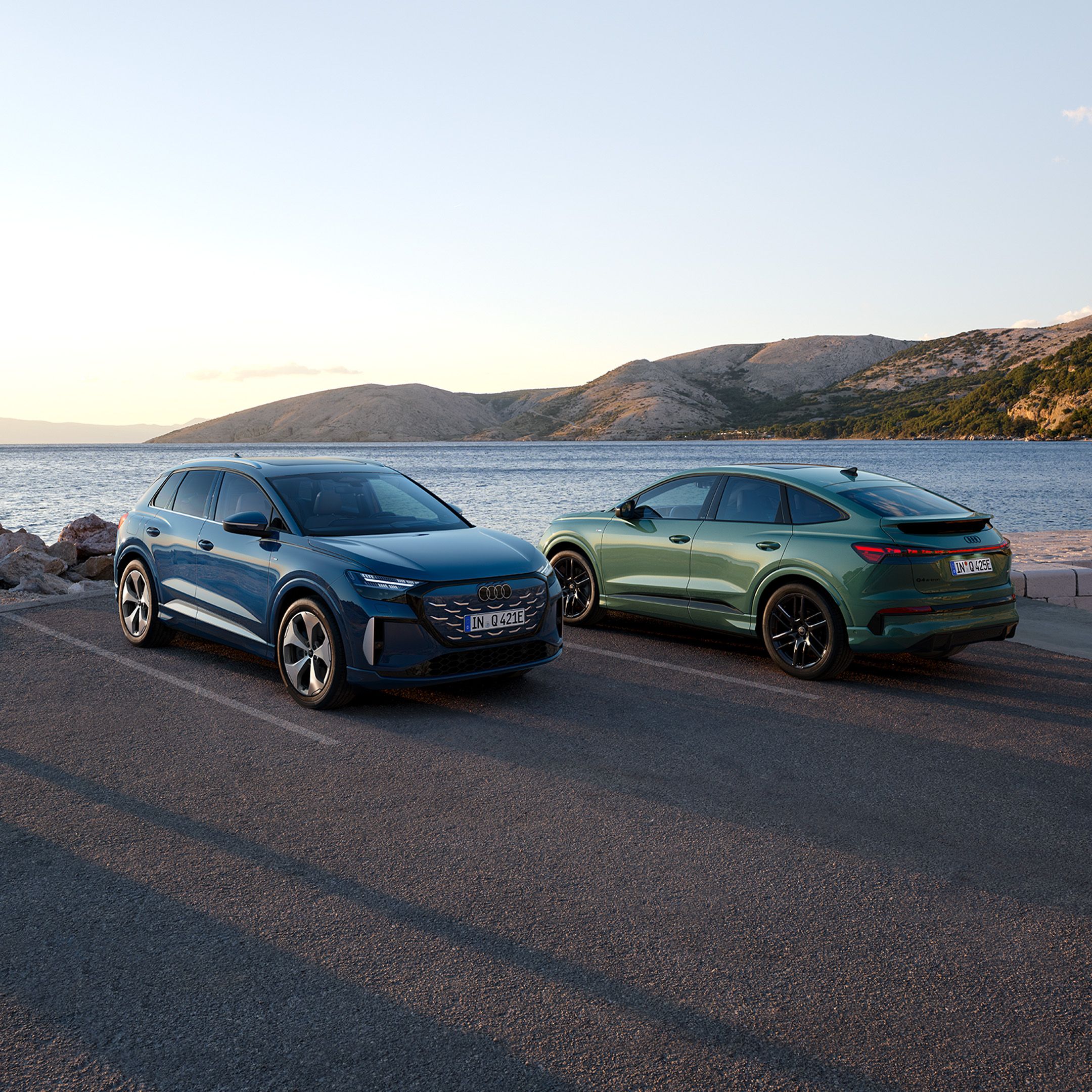 Q4 SUV e-tron quattro performance și Q4 Sportback e-tron quattro performance parcate pe un drum de coastă, cu marea și munții în fundal.