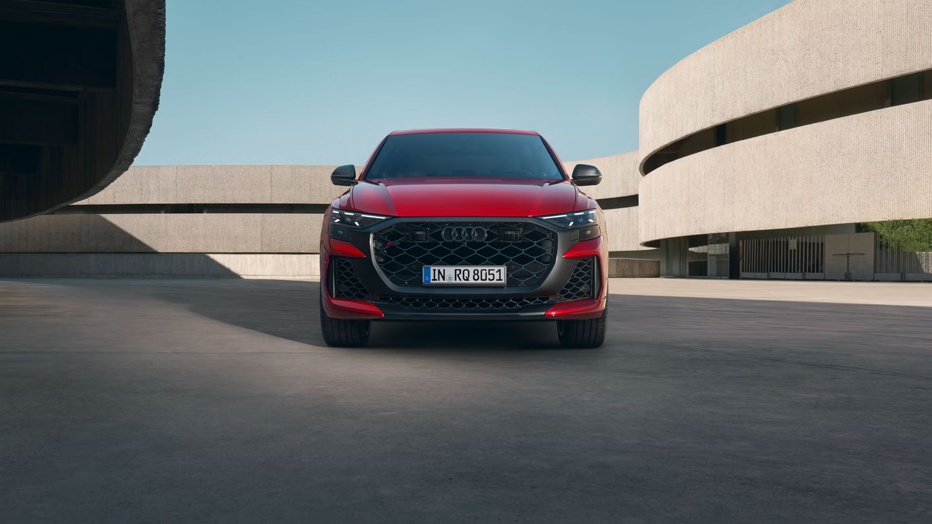 Der RS Q8 SUV performance in Chilirot Metallic von vorne parkend vor einem futuristischen Gebäude.