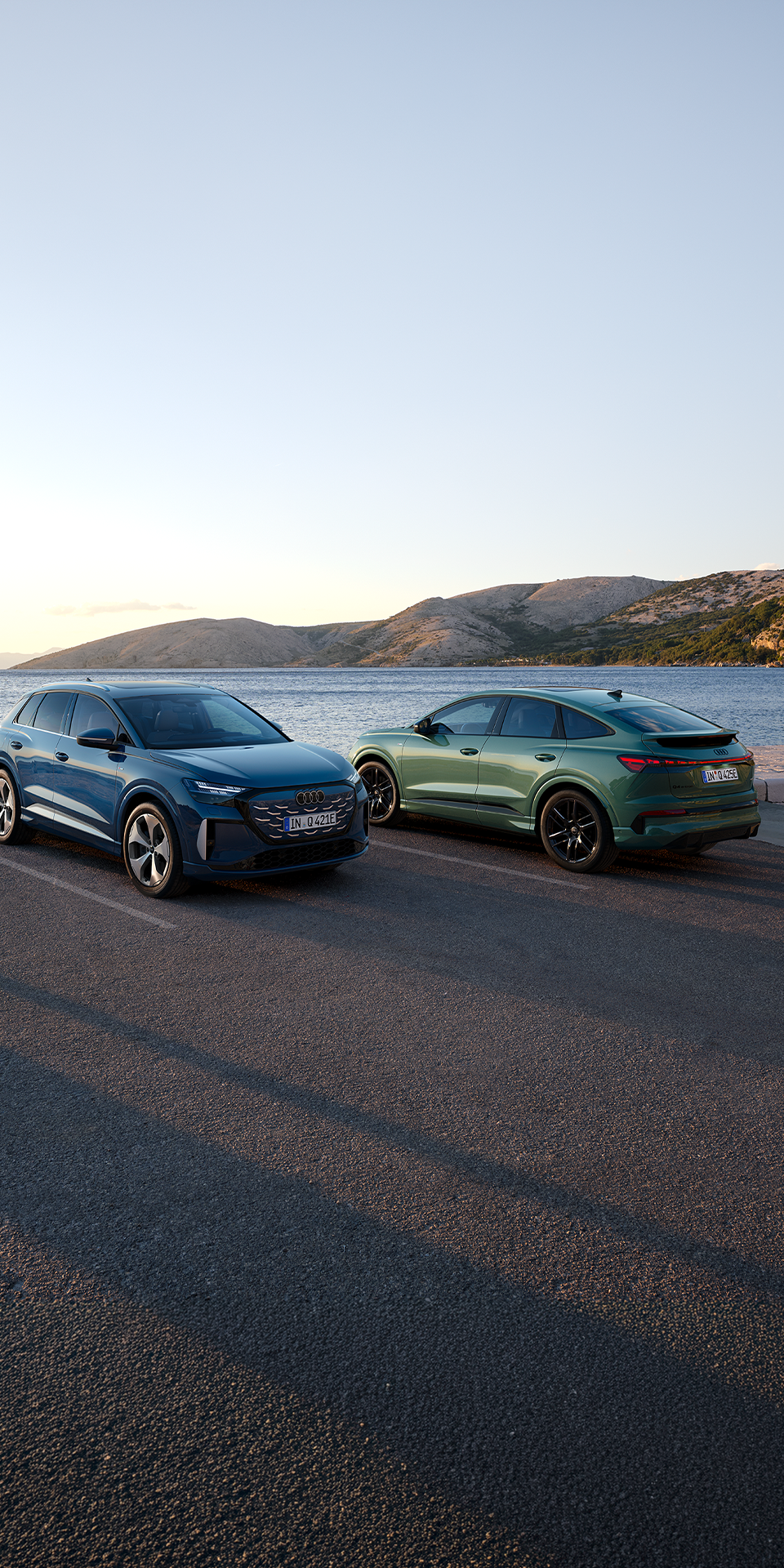 Q4 SUV e-tron quattro performance și Q4 Sportback e-tron quattro performance parcate pe un drum de coastă, cu marea și munții în fundal.