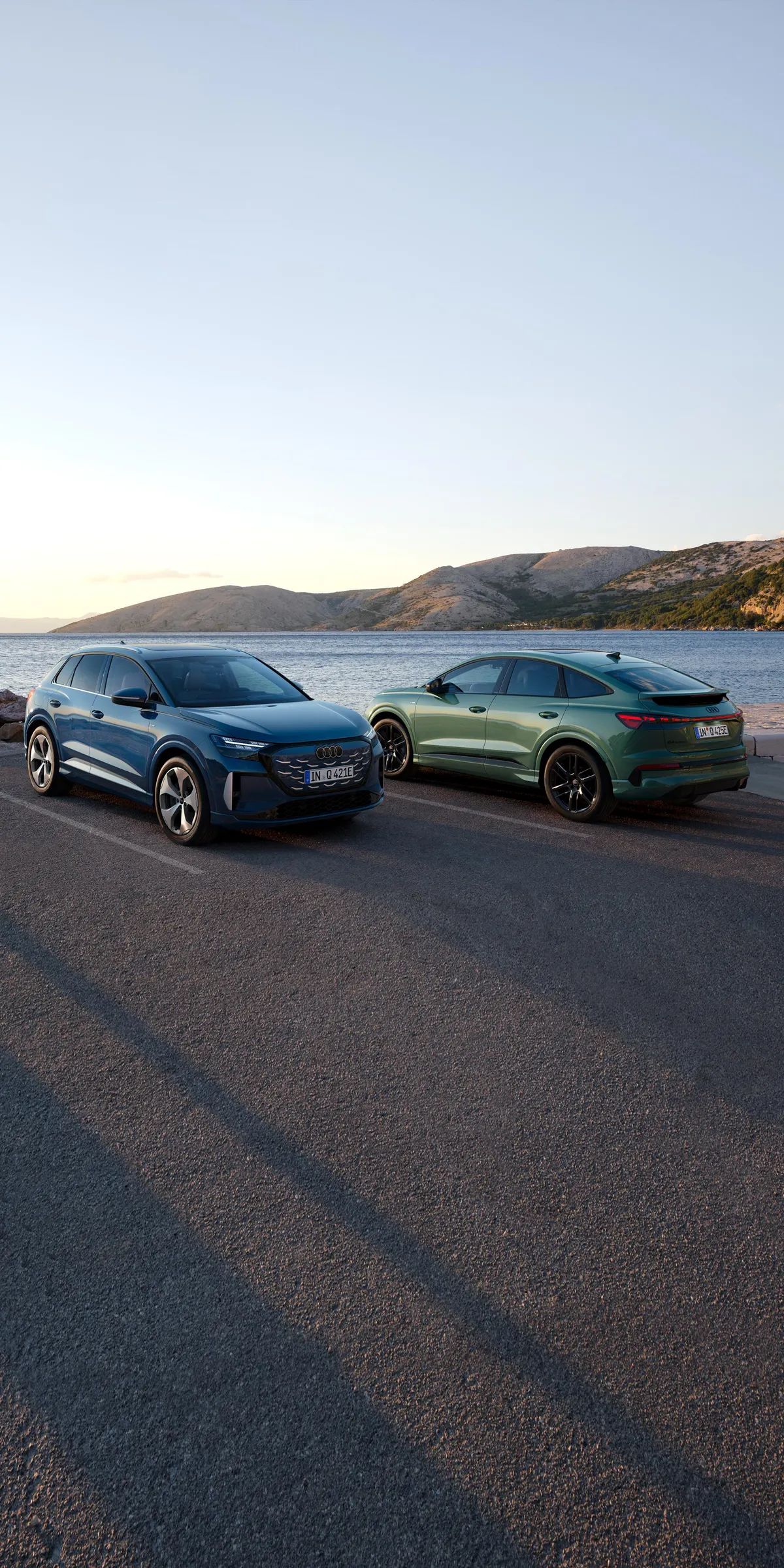 Q4 SUV e-tron quattro performance și Q4 Sportback e-tron quattro performance parcate pe un drum de coastă, cu marea și munții în fundal.