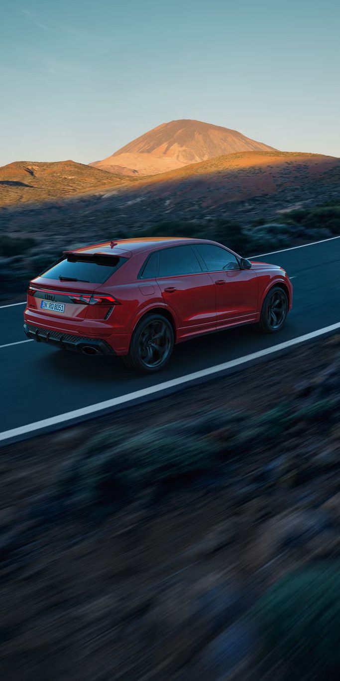 Der RS Q8 SUV performance von schräg hinten auf einer Bergstraße. Die Sonne beleuchtet die felsige Landschaft im Hintergrund, das Fahrzeug im Schatten.
