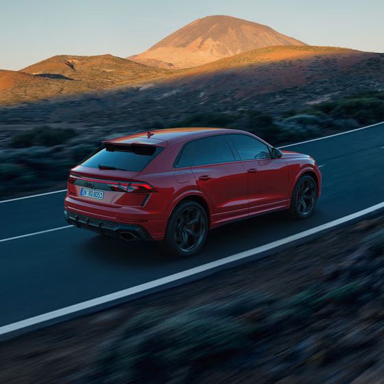 Der RS Q8 SUV performance von schräg hinten auf einer Bergstraße. Die Sonne beleuchtet die felsige Landschaft im Hintergrund, das Fahrzeug im Schatten.