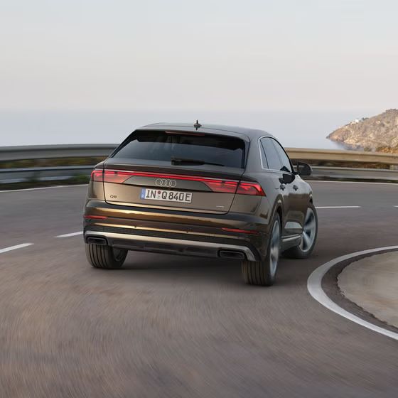 Der Q8 SUV e-hybrid von hinten passiert eine Kurve auf einer Bergstraße, links das Meer.