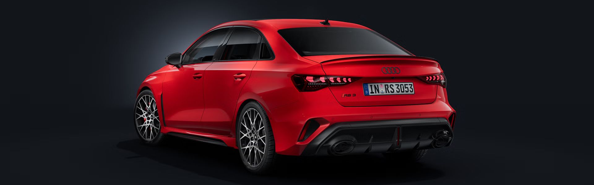 Die Audi RS 3 Limousine schräg von hinten auf dunklem Hintergrund.