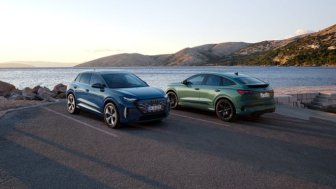 Q4 SUV e-tron quattro performance și Q4 Sportback e-tron quattro performance parcate pe un drum de coastă, cu marea și munții în fundal.