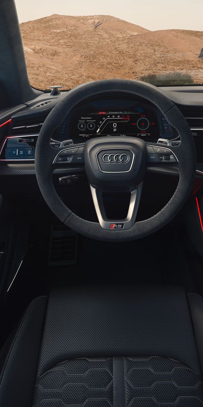 Blick von hinten auf das Cockpit des RS Q8 SUV mit Fokus auf das Lenkrad und die digitalen Displays. Durch die Windschutzscheibe sind karge Felsen zu erkennen.