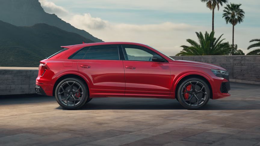 Der RS Q8 SUV performance von der Seite parkend. Die Mauer dahinter begrenzt das Grundstück, Palmen auf der rechten und hochaufragende Berge auf der linken Seite.