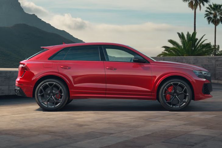 Der RS Q8 SUV performance von der Seite parkend. Die Mauer dahinter begrenzt das Grundstück, Palmen auf der rechten und hochaufragende Berge auf der linken Seite.