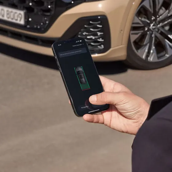 Eine männliche Hand hält ein Smartphone, auf dem Display ist ein Fahrzeug zu erkennen. Der Mann steht vor einem Q8 SUV, der im Anschnitt zu sehen ist.