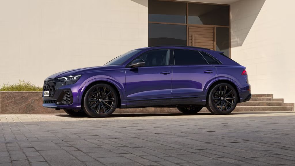 Der Q8 SUV in Individuallackierung Samtviolett von der Seite, parkend vor einem modernen Gebäude.