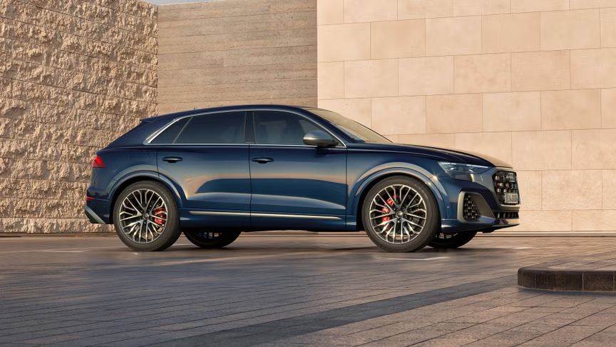 Der Audi SQ8 SUV in Seitenansicht auf einem Parkplatz, umrahmt von hohen Mauern.