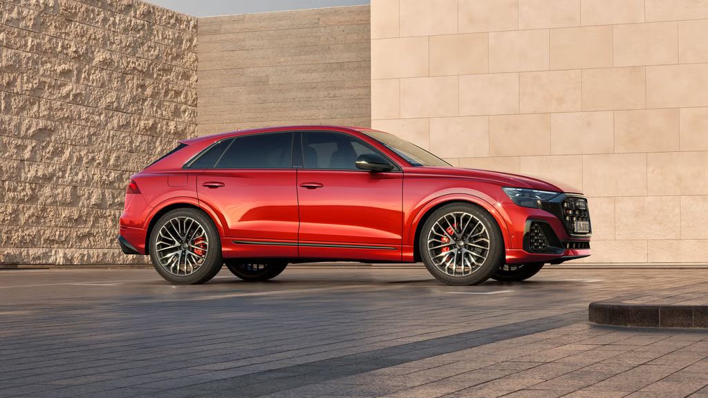 Der SQ8 SUV mit Individuallackierung Audi exclusive in Misanorot Perleffekt in Seitenansicht auf einem Parkplatz, umrahmt von hohen Mauern.
